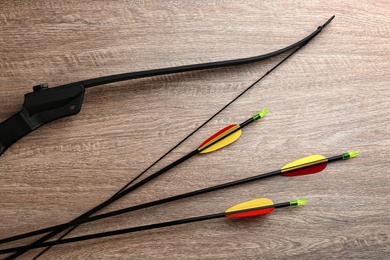 Photo of Plastic arrows and bow on wooden table, flat lay. Archery sports equipment