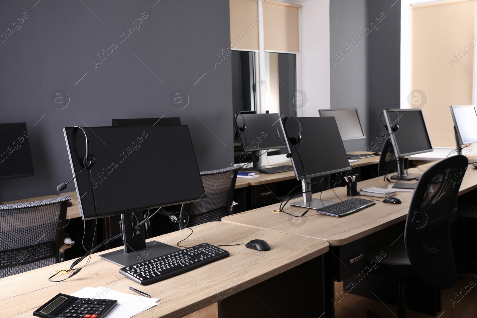 Photo of Modern computers with headsets on wooden desk in office. Hotline service