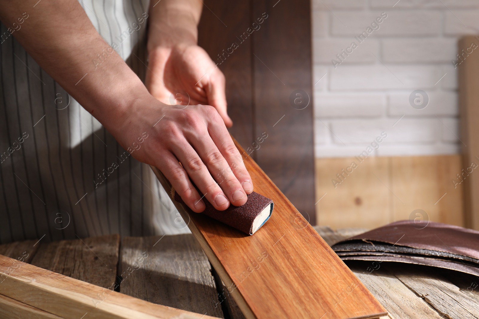 Photo of Man polishing wooden plank with sandpaper at table indoors, closeup