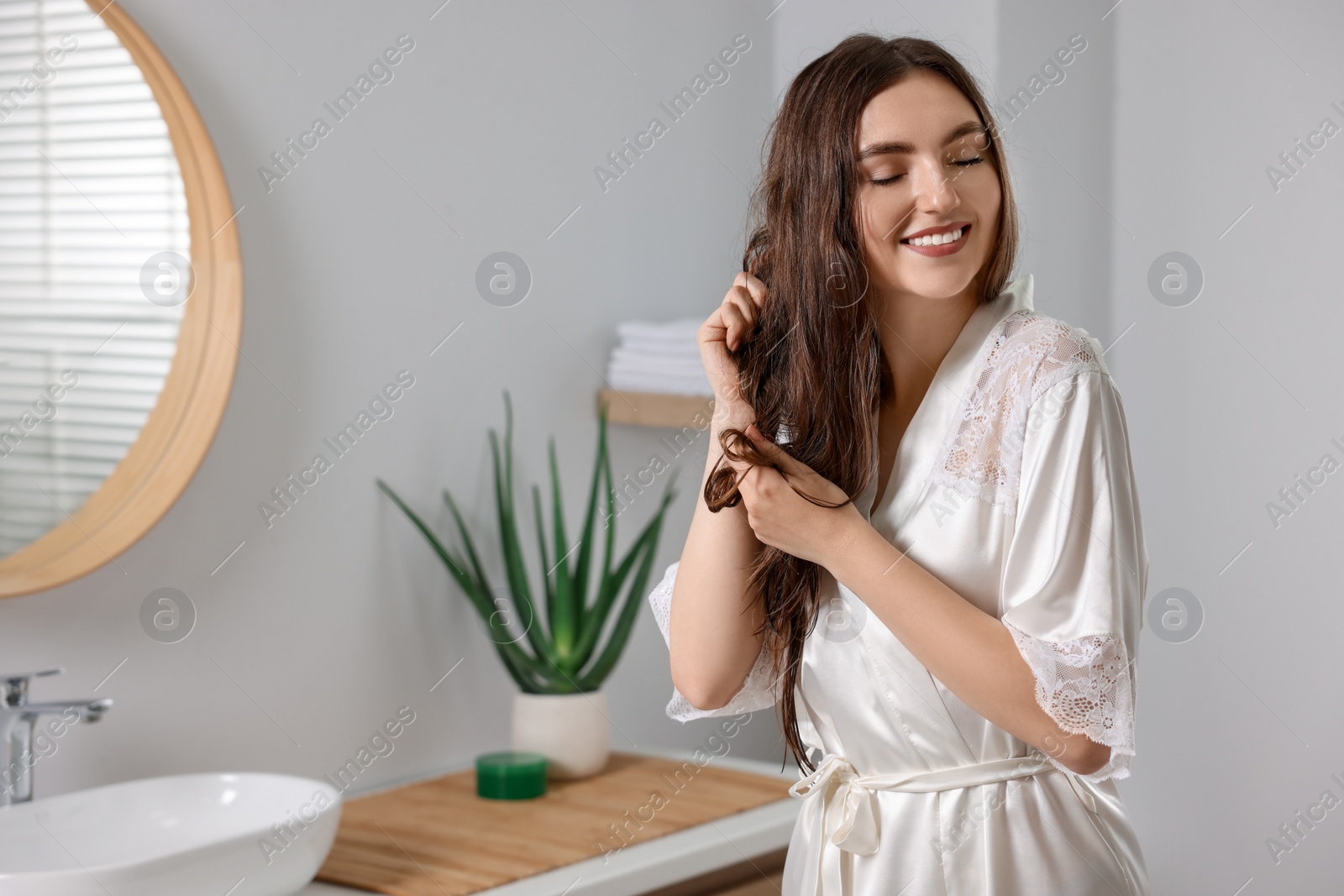 Photo of Young woman applying cosmetic hair mask in bathroom. Space for text