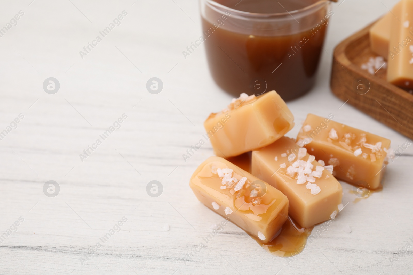 Photo of Yummy caramel candies, sauce and sea salt on white wooden table, closeup. Space for text