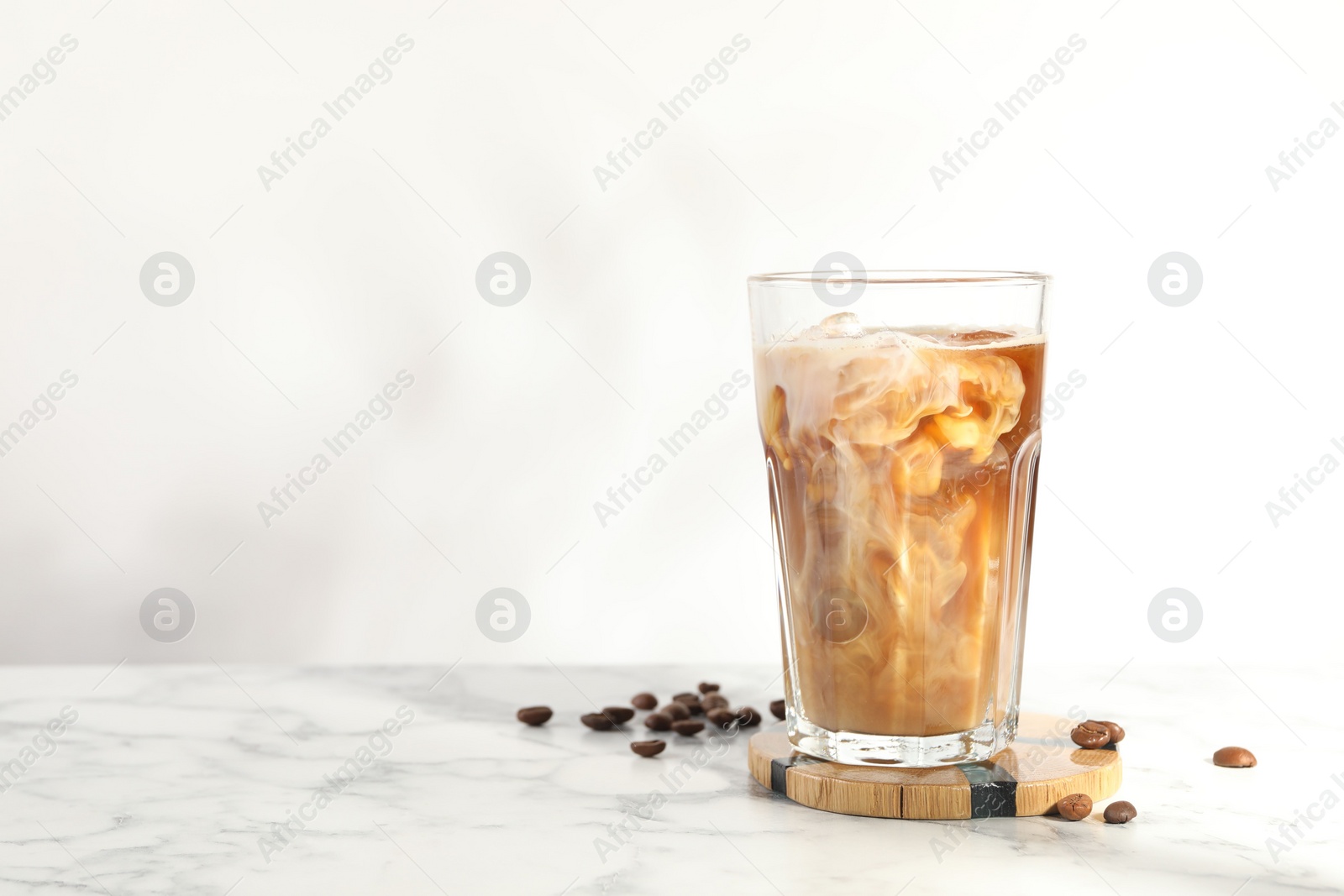 Photo of Refreshing iced coffee with milk in glass and beans on white marble table, space for text