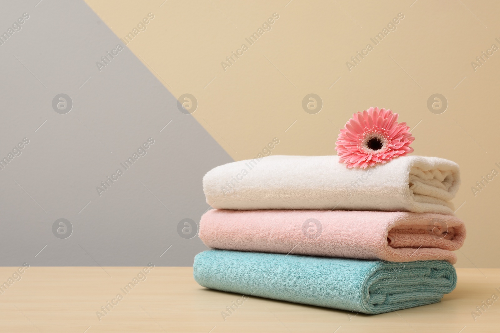 Photo of Stack of fresh towels with flower on table. Space for text