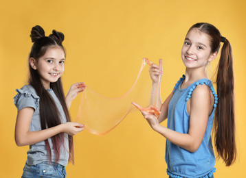 Happy girls with slime on yellow background