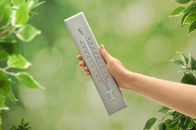 Photo of Woman with weather thermometer on blurred background, closeup