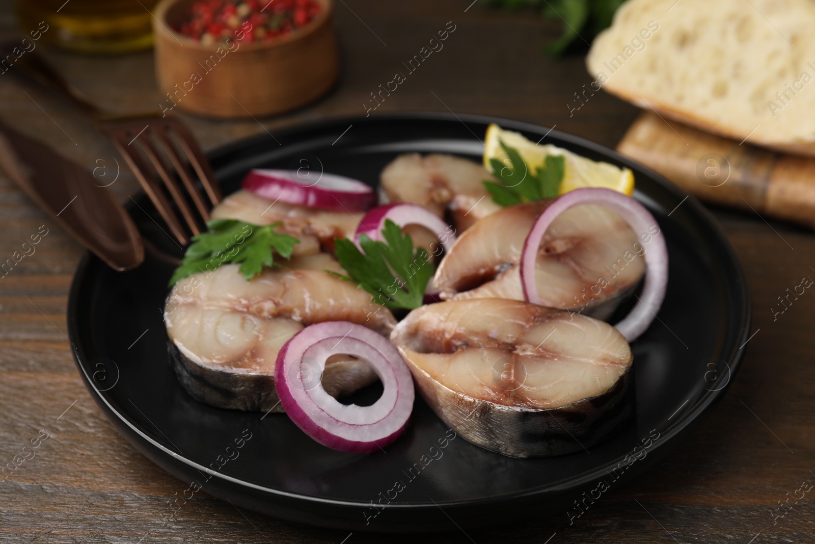 Photo of Slices of tasty salted mackerel, onion rings and parsley on wooden table, closeup