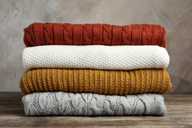 Photo of Stack of warm clothes on wooden table against grey background. Autumn season