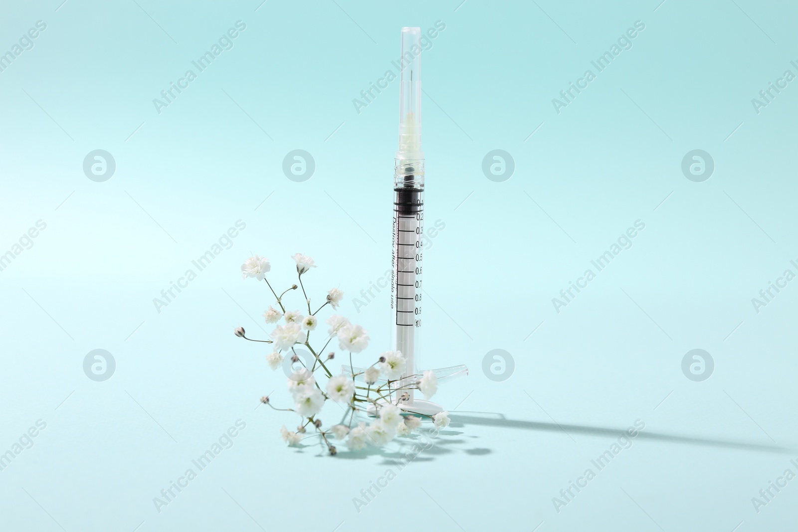 Photo of Cosmetology. Medical syringe and gypsophila on light blue background