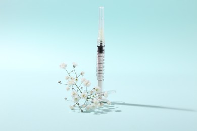 Photo of Cosmetology. Medical syringe and gypsophila on light blue background