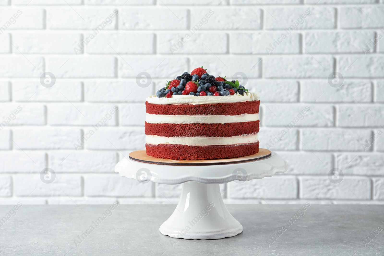 Photo of Stand with delicious homemade red velvet cake near brick wall