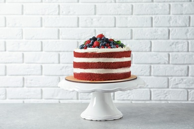 Photo of Stand with delicious homemade red velvet cake near brick wall