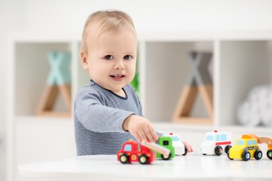 Children toys. Cute little boy playing with toy cars at white table in room, space for text