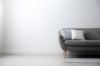 Photo of Grey sofa with pillows near white wall in stylish living room interior. Space for text