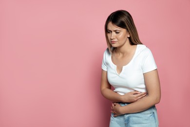 Young woman suffering from menstrual pain on pink background, space for text
