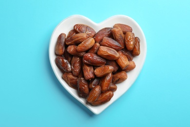 Photo of Heart shaped plate with sweet dried date fruits on color background, top view
