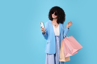 Photo of Happy young woman with shopping bags and modern smartphone on light blue background. Space for text