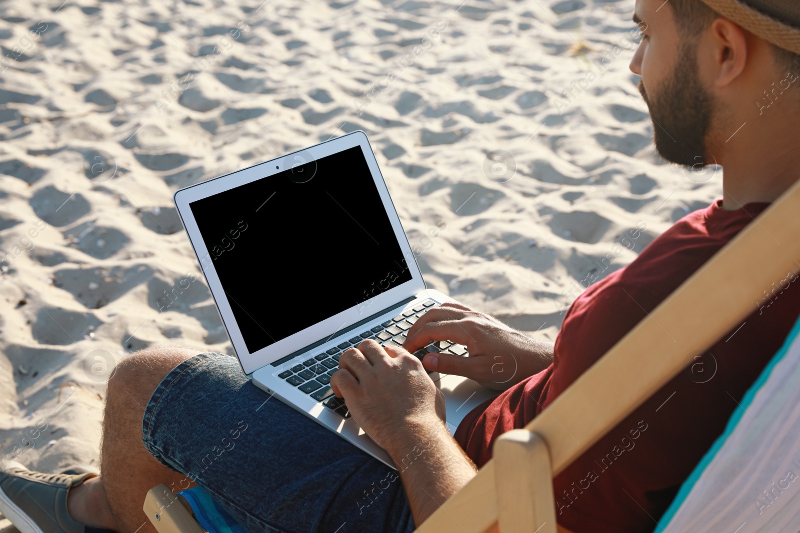 Photo of Man working with laptop in deck chair on beach, closeup