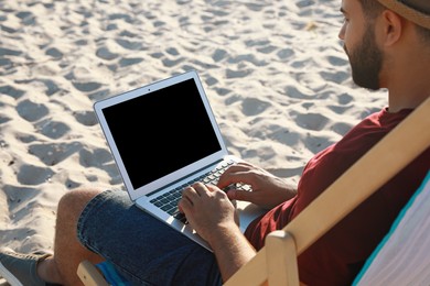 Man working with laptop in deck chair on beach, closeup