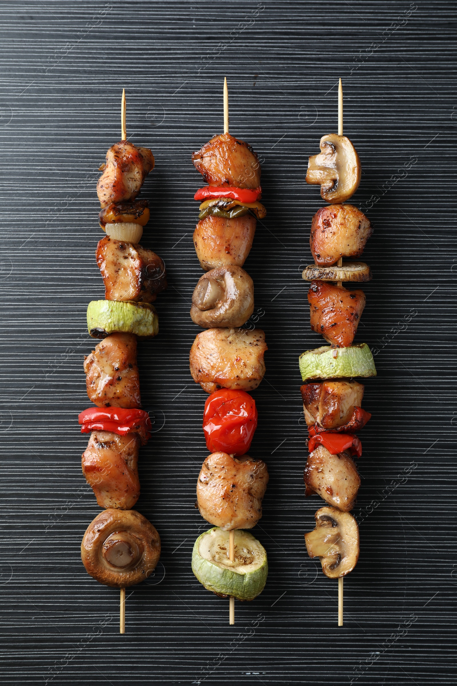 Photo of Delicious shish kebabs with vegetables on black table, top view