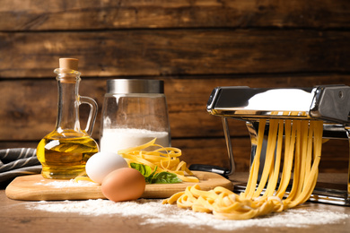Photo of Pasta maker machine with dough and products on wooden table