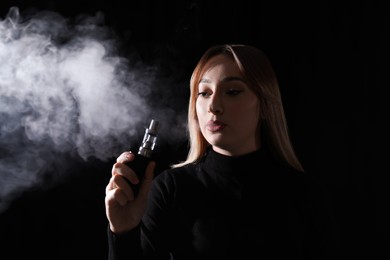 Photo of Young woman using electronic cigarette on black background
