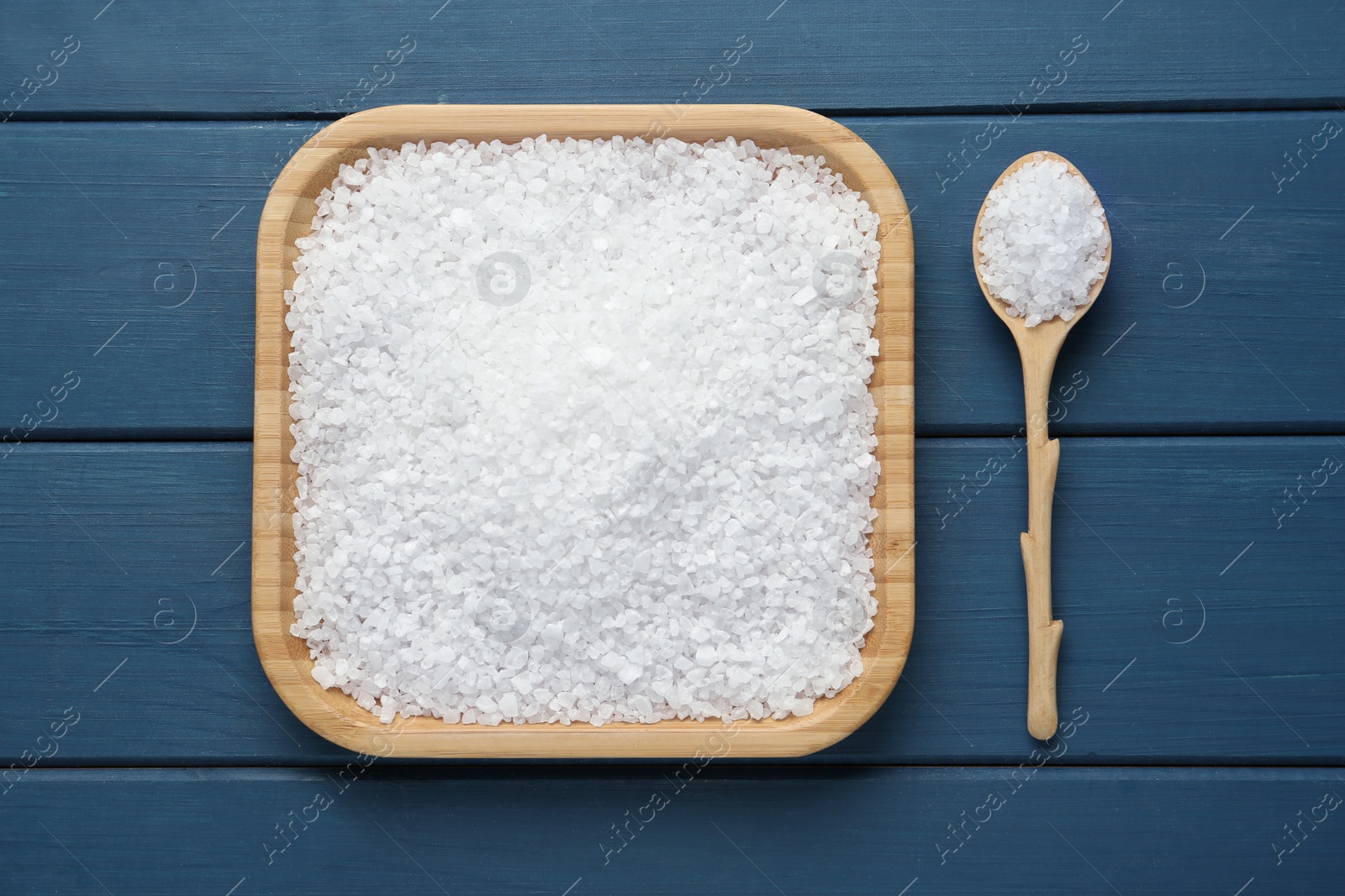 Photo of Plate and spoon with natural sea salt on blue wooden table, flat lay