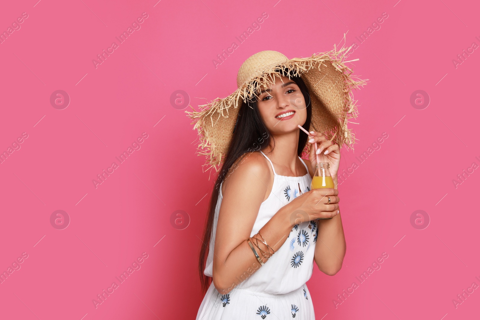 Photo of Beautiful young woman with straw hat and bottle of refreshing drink on pink background. Space for text