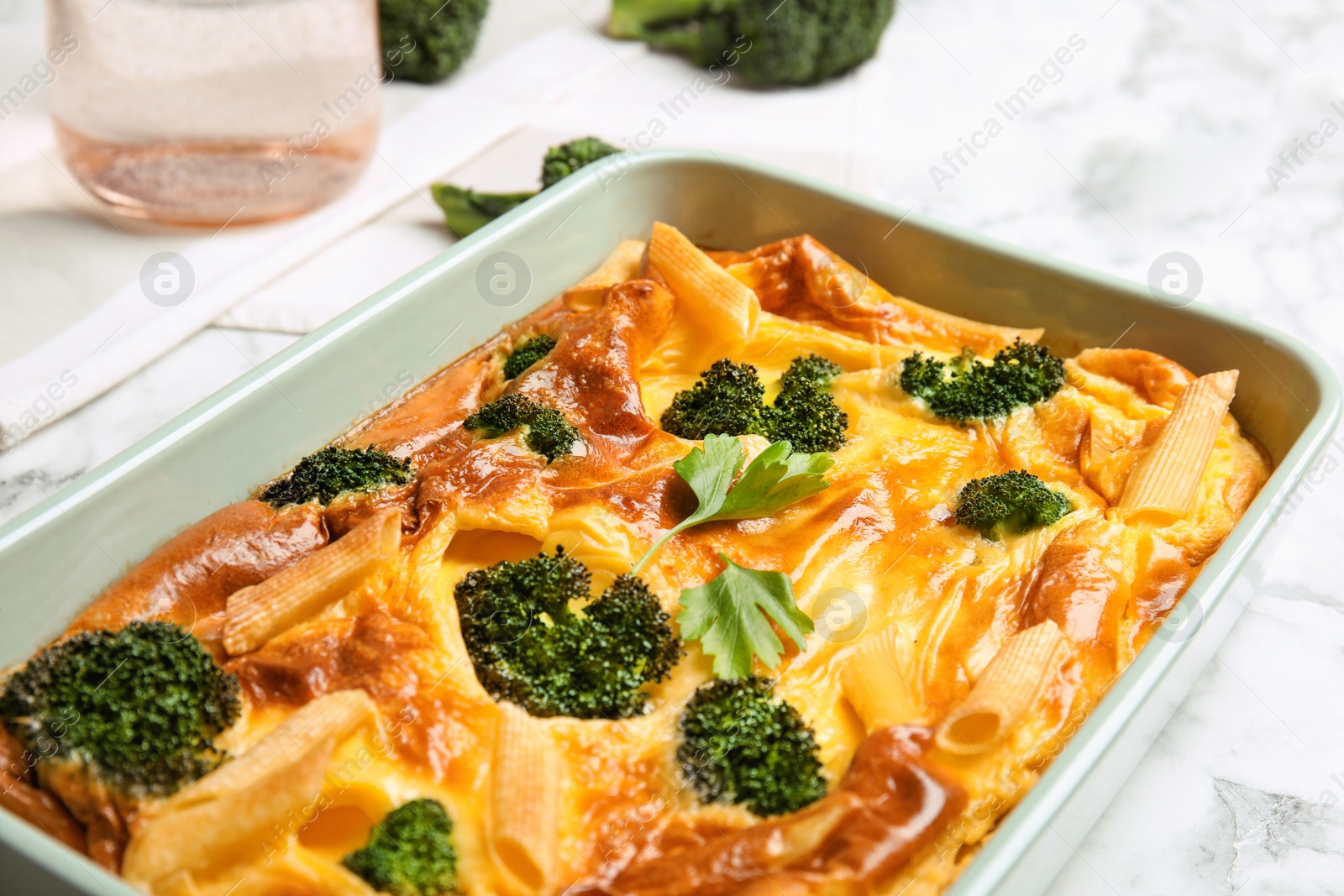 Photo of Tasty broccoli casserole in baking dish on white marble table, closeup