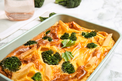 Photo of Tasty broccoli casserole in baking dish on white marble table, closeup