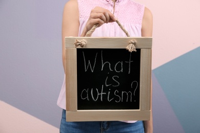 Photo of Woman holding blackboard with phrase "What is autism?" on color background