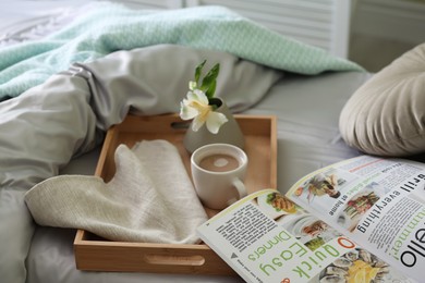 Photo of Cup of coffee, flower and magazine on bed with fresh linens indoors