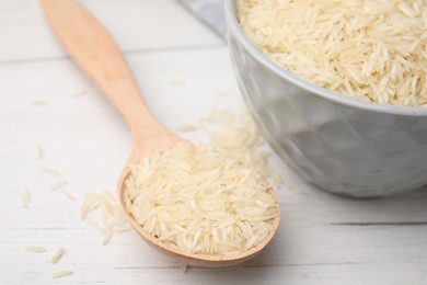 Spoon and bowl with raw rice on white wooden table, closeup