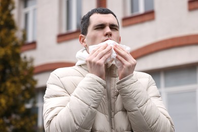 Photo of Sick young man with tissue on city street. Cold symptoms