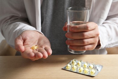 Photo of Man with glass of water and pill at wooden table, closeup