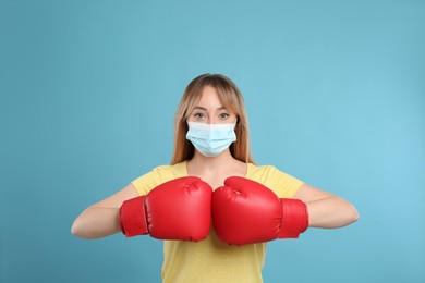 Photo of Woman with protective mask and boxing gloves on light blue background. Strong immunity concept
