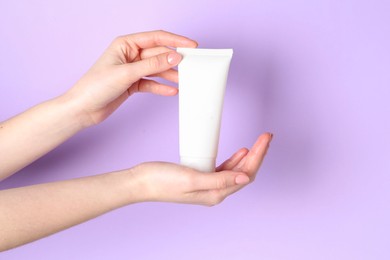 Woman holding tube of cream on violet background, closeup