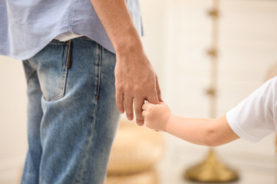 Photo of Father holding hands with his child indoors, closeup. Happy family