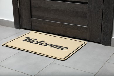 Photo of Beautiful beige doormat with word Welcome on floor near entrance