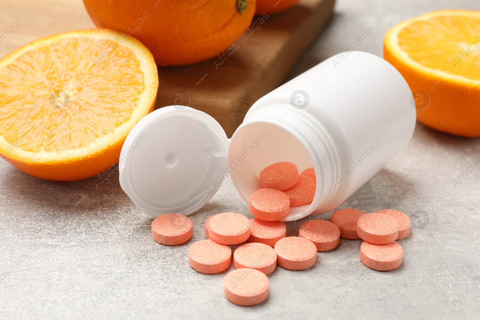 Photo of Dietary supplements. Overturned bottle, pills and oranges on grey table