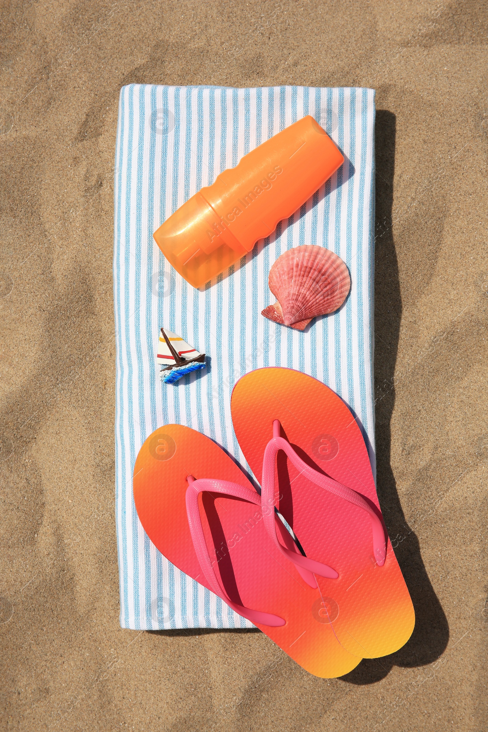 Photo of Bottle of sunscreen, flip flops and towel on sand, top view. Sun protection care