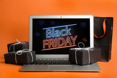 Photo of Laptop with Black Friday announcement, shopping bag and gifts on orange background