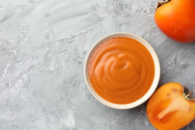 Photo of Delicious persimmon jam and fresh fruits on grey table, flat lay. Space for text