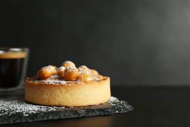 Photo of Delicious tart with hazelnuts, sweet caramel and powdered sugar on black table. Space for text