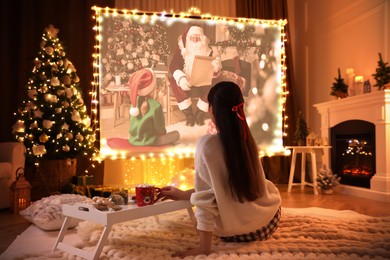 Image of Woman watching Christmas movie via video projector in room. Cozy winter holidays atmosphere