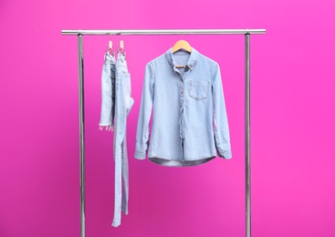 Photo of Rack with stylish jeans and denim clothes on color background