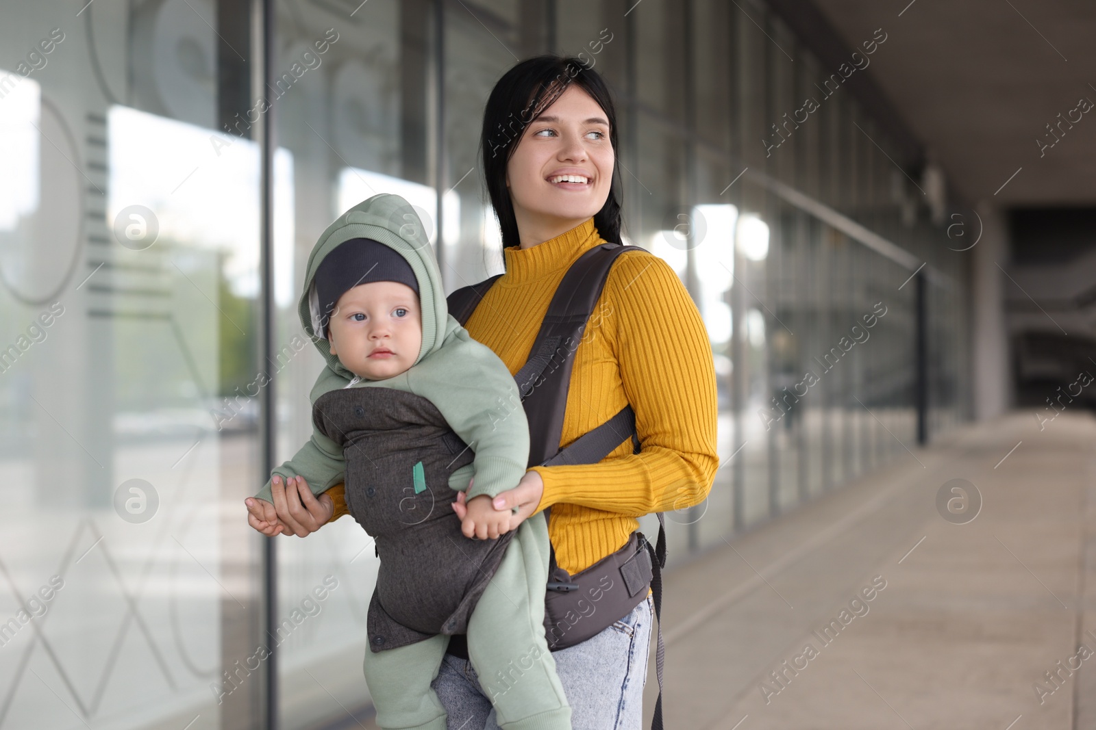 Photo of Mother holding her child in sling (baby carrier) near building outdoors