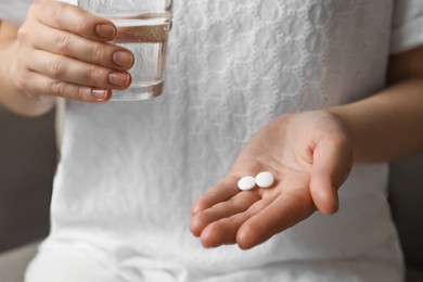 Woman holding glass of water and pills indoors, closeup. Menopause concept