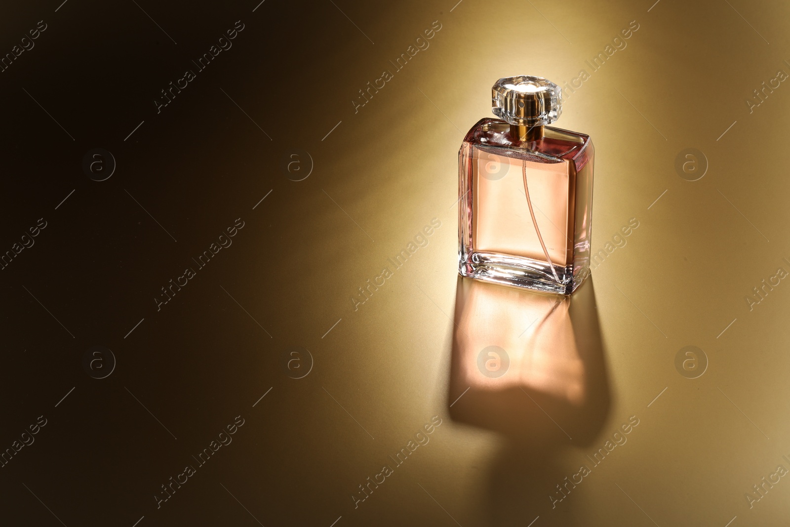 Photo of Luxury women's perfume. Sunlit glass bottle on golden background, space for text