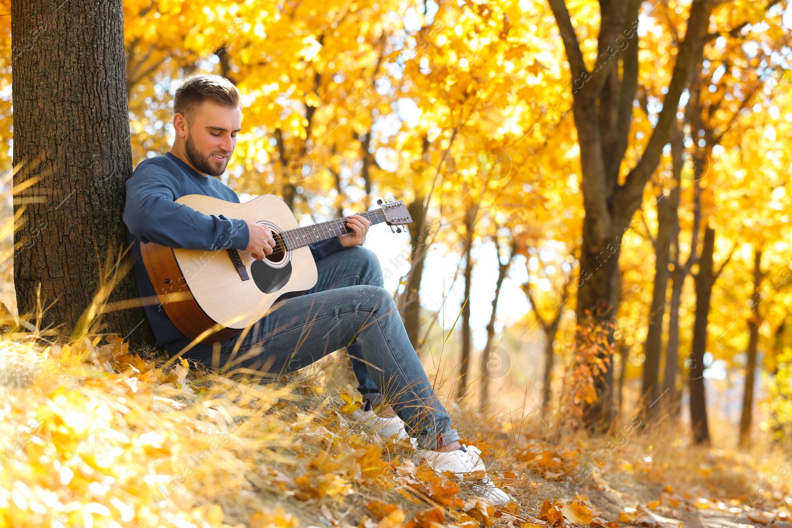 Photo of Young man playing guitar in autumn park