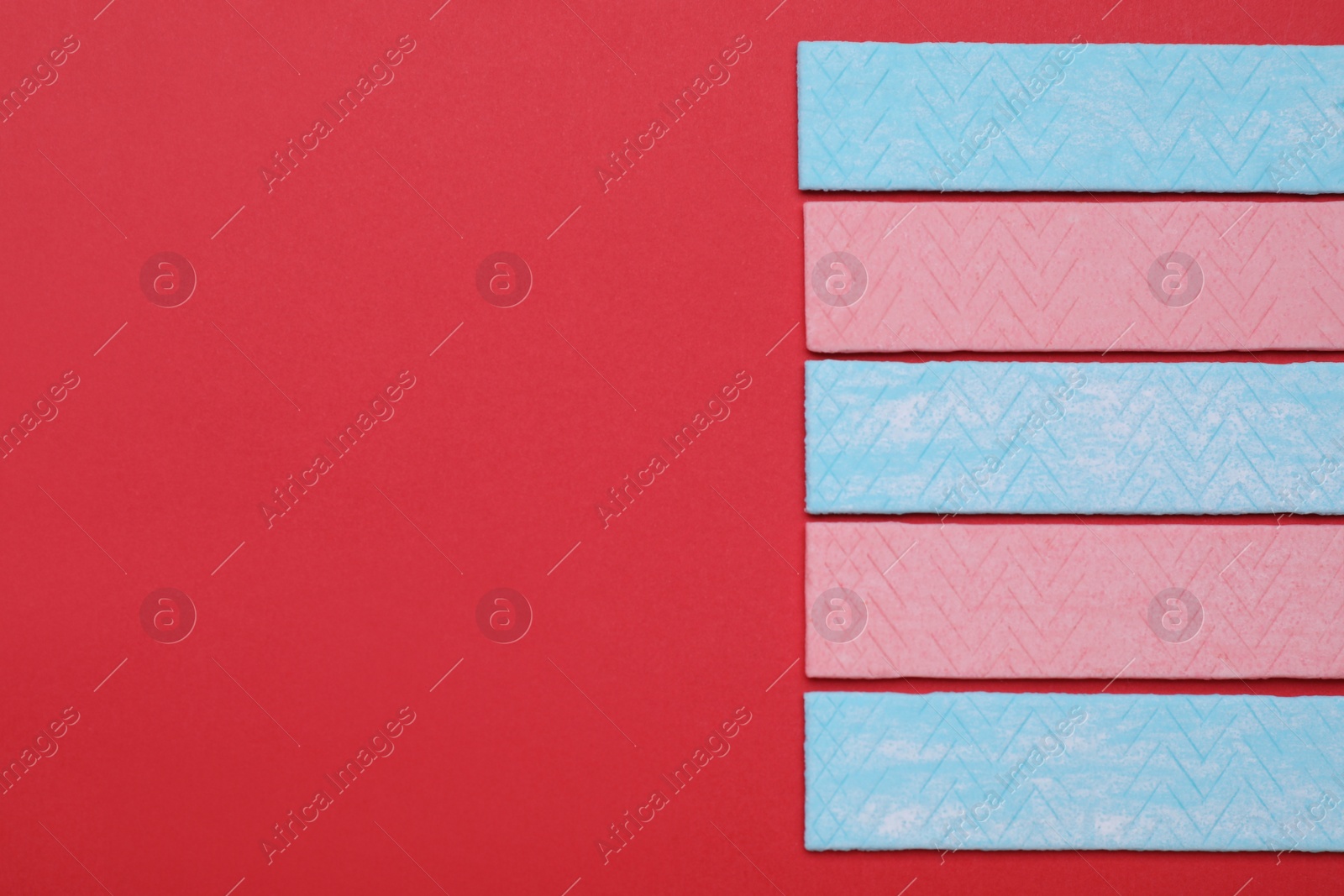Photo of Sticks of tasty chewing gum on red background, flat lay. Space for text